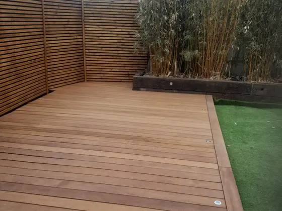 Finished hardwood deck laid tight to a slatted fence, with recessed lights set into the edge