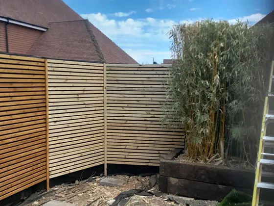 Modern slatted fencing run around a raised sleeper bed and established bamboo